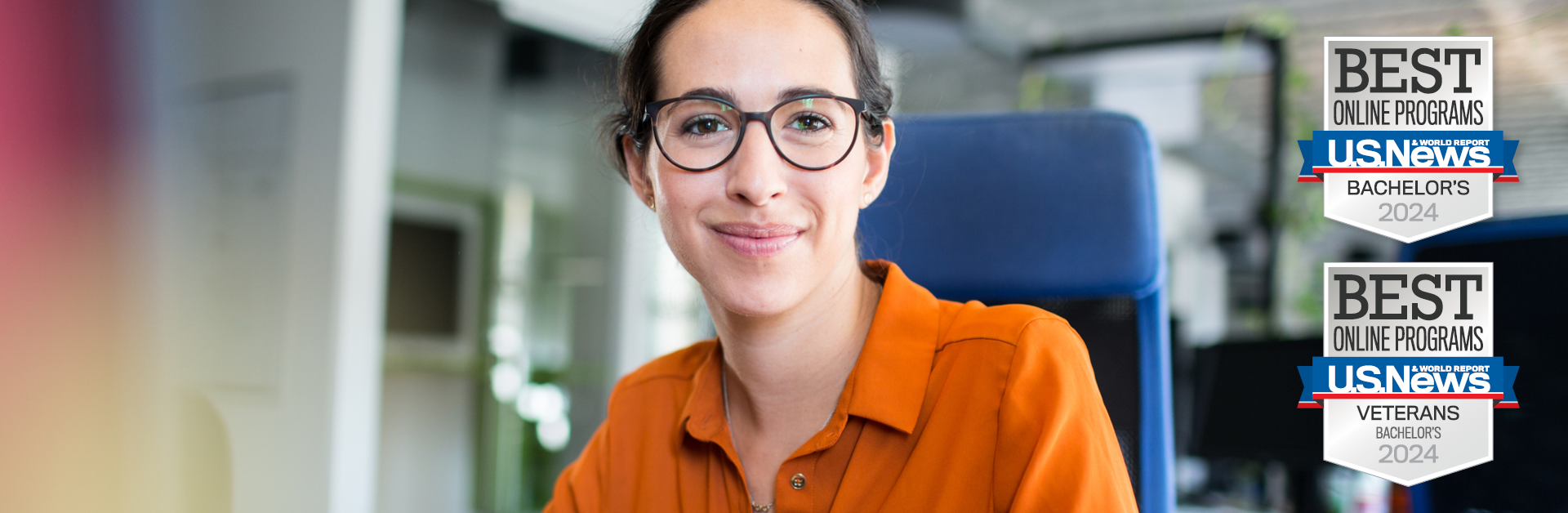 a white woman with brown hair wearing glasses and an orange shirt sitting in an office chair