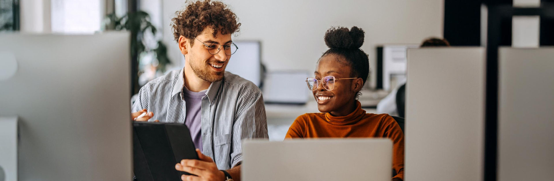 a man and woman sitting next to each other working on laptops