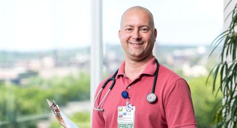 Smiling healthcare worker with a stethoscope standing in front of glass windows with a view of a landscape behind them