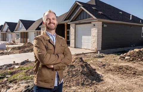 middle aged white man wearing a tan jacket standing in front of a row of houses