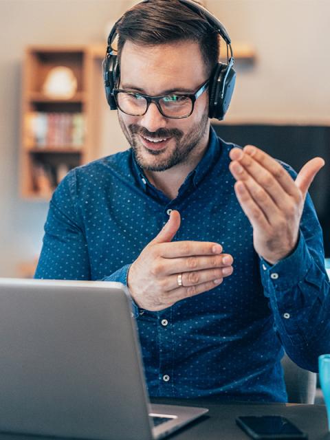 Person wearing headphones talking and gesturing with their hands in front of an open laptop computer