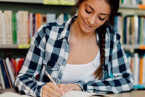 A girl with a braid wearing a flannel writing in a notebook