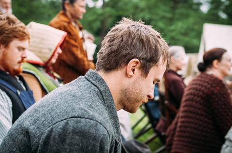 Person at an outdoor alumni event sitting in a chair on a lawn and listening to a presentation