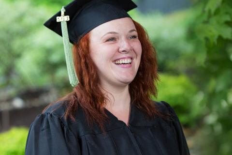 happy smiling graduate in a graduation gown and mortarboard with a green tassle