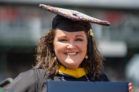 Smiling woman in graduation cap and gown holding diploma