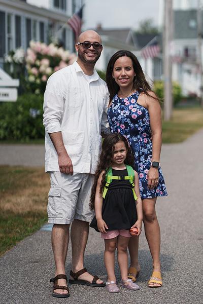 a family photo outside with a young girl standing in front of a man and woman