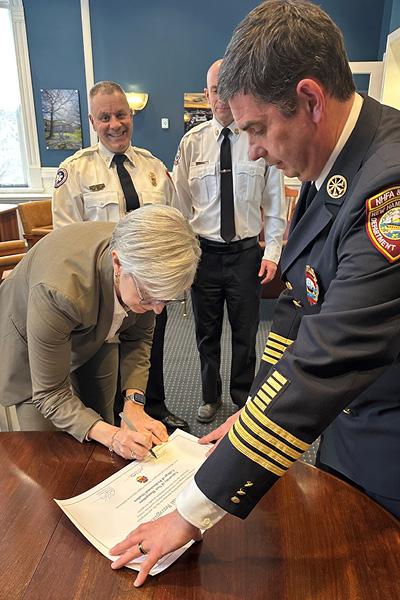 a fireman standing next to a woman signing a document on a table